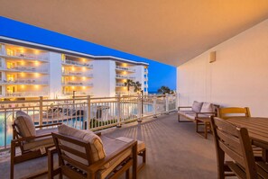 A hotel balcony with a pool, outdoor seating, and a view of the ocean at dusk. - Two-bedroom with bunks, balcony overlooking pool & on-site pickleball (Santa Rosa Beach)