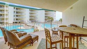 En balkong med möbler i rotting, med utsikt över en pool och en hotellbyggnad med flera balkonger.