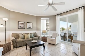 Un salon comprenant un canapé, un fauteuil et une table basse, un ventilateur de plafond et une vue sur un balcon.