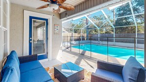 Eine überdachte Terrasse mit Korbmöbeln, einem Deckenventilator und Blick auf einen Swimmingpool.