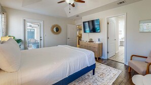 Ein Schlafzimmer mit einem Bett, einem Deckenventilator, einem Fernseher, einer Kommode und einer Tür zu einem anderen Raum.