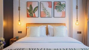 Une chambre d’hôtel avec un lit, du linge de lit blanc, une tête de lit et trois tableaux représentant des plantes, accrochés au mur.