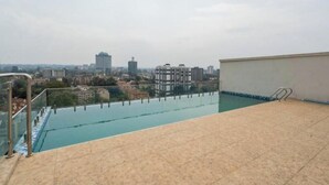 Une piscine sur le toit offrant une vue sur la ville, avec une balustrade en verre et un sol carrelé.