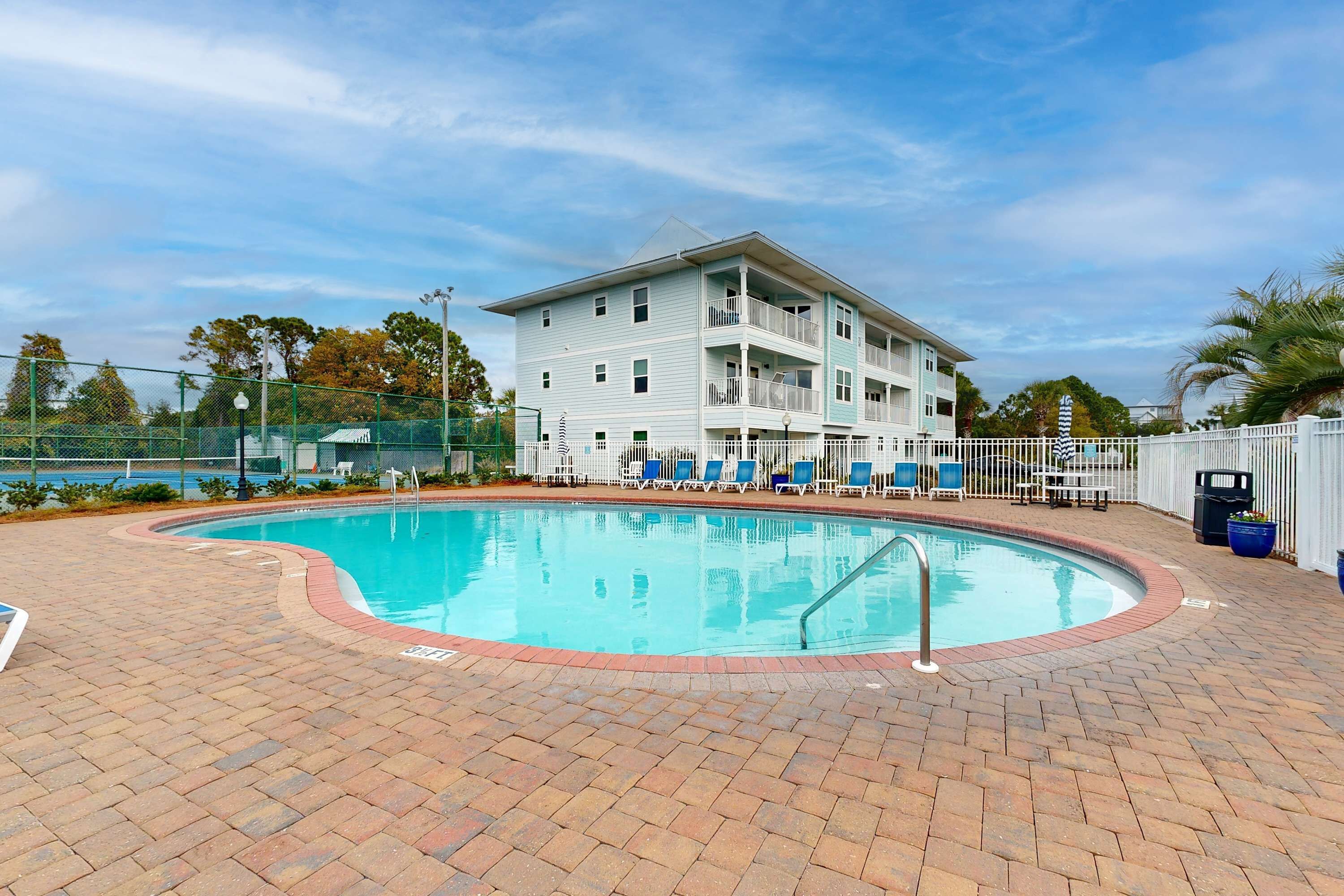 A pool area with a brick patio, lounge chairs, and a multi-story building with balconies.