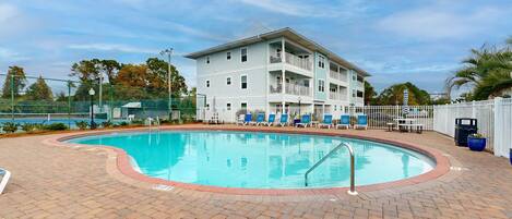 A pool area with a brick patio, lounge chairs, and a multi-story building with balconies.