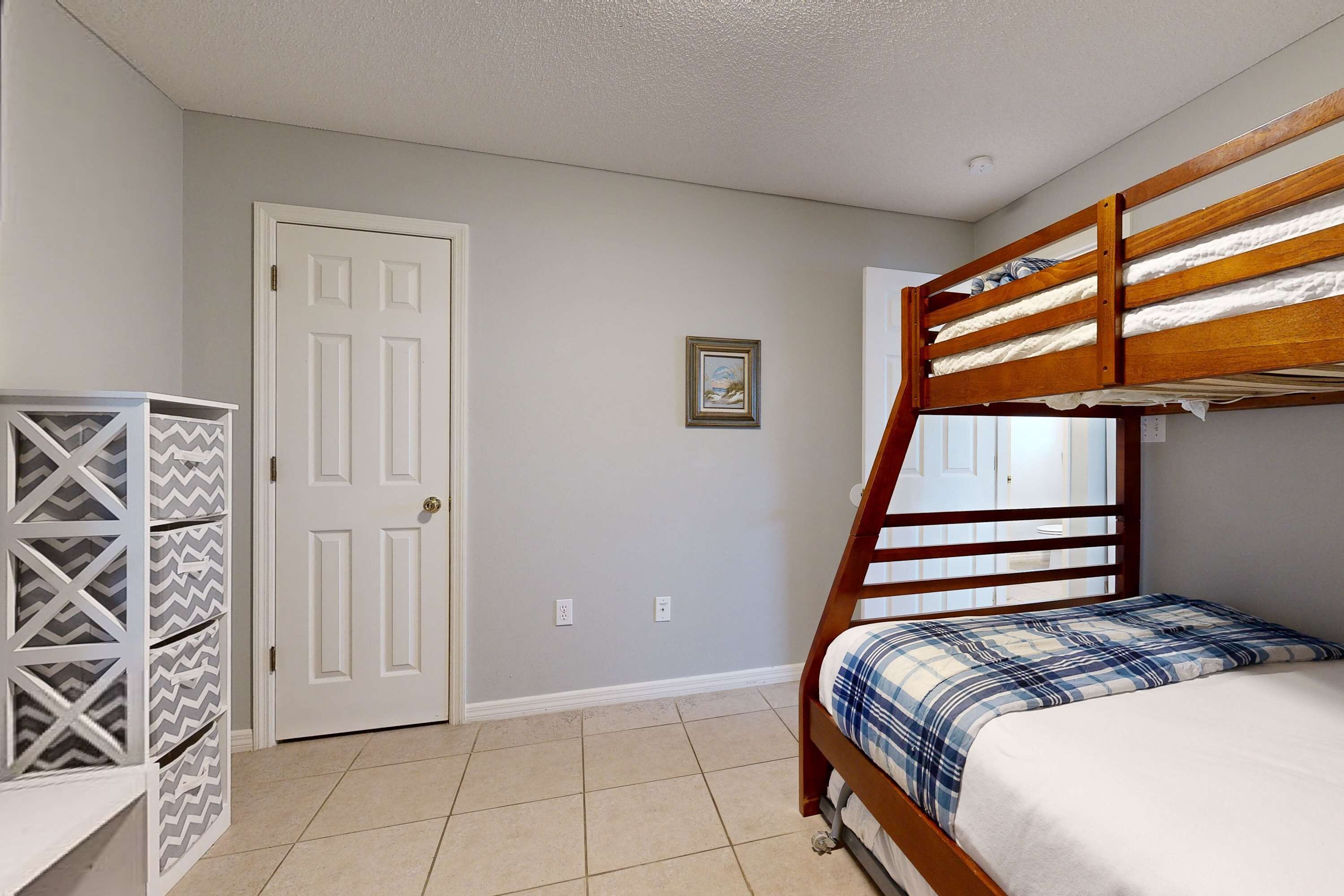 Une chambre avec un lit superposé, une porte, un tableau encadré et un meuble de rangement avec des portes à motifs.