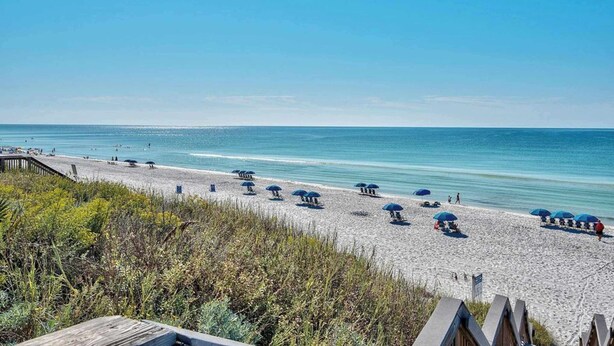 A beach with umbrellas and beach chairs, a wooden walkway, and a clear view of the ocean. - Gorgeous, private, coastal home with a shared pool, fitness room (Santa Rosa Beach)