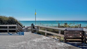 A wooden boardwalk leading to a beach with a flag. - Gorgeous, private, coastal home with a shared pool, fitness room (Santa Rosa Beach)