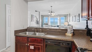A kitchen with granite countertops, a dishwasher, and a view of the living area. - Bright Gulf-front condo with two balconies, pool, central AC, & W/D (Panama City Beach)