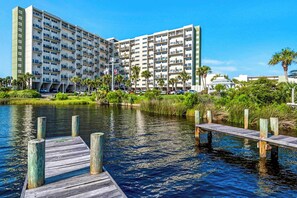 A multi-story hotel with balconies, a dock extending into a body of water, and surrounding greenery. - Great Pinnacle Port villa with lots of character & balcony - steps from beach (Panama City Beach)