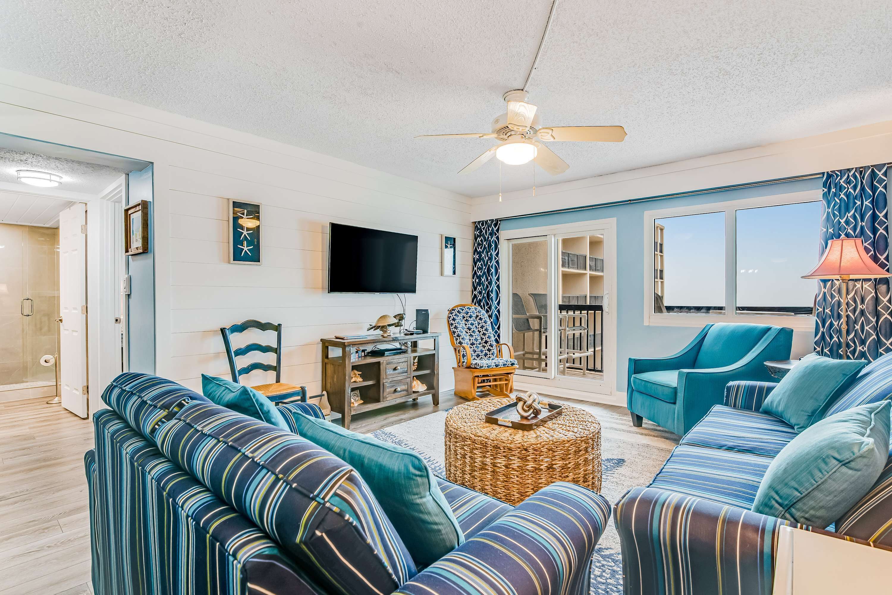 A living room with striped sofas, a ceiling fan, a TV, and a patterned wall.
