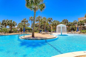 Une piscine bordée de palmiers, avec des chaises longues et une fontaine.