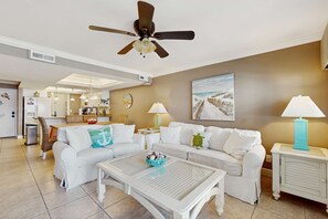 A living room with a ceiling fan, white sofas, a coffee table, and a dining area in the background. - Gorgeous beachfront condo, shared pool and beach access (Panama City Beach)