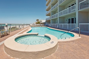 Ein Schwimmbecken mit Whirlpool, umgeben von einer Pflasterterrasse und einem weißen Balkon mit Geländern.