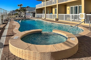 A swimming pool with a hot tub, surrounded by a white fence and a building with balconies. - Deluxe condo with Gulf view, heated pool & balcony (Panama City Beach)