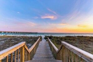 A wooden boardwalk leading to a beach with a pier in the background. - Bayview condo with pool, hot tub, and private balcony (Panama City Beach)