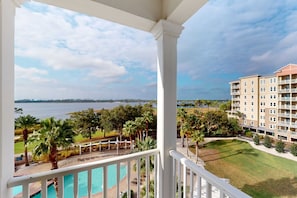 A balcony with a view of a swimming pool, palm trees, and a distant body of water. - Bayview condo with pool, hot tub, and private balcony (Panama City Beach)