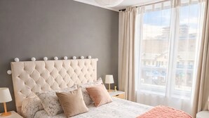 A bedroom with a tufted headboard, a floral bedspread, a peach throw blanket, and a view of the city through large windows. - Central and modern apartment in Temuco.Cowork/gym/lavandería entrance by Safecard. (Cautin)