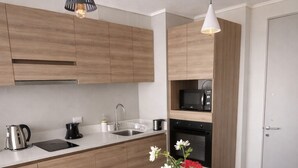 A modern kitchen with wooden cabinets, a white countertop, a round dining table with white chairs, and two pendant lights. - Central and modern apartment in Temuco.Cowork/gym/lavandería entrance by Safecard. (Cautin)
