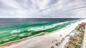 Uma praia com águas turquesa cristalinas, uma faixa de areia e um cais que se estende para o mar.