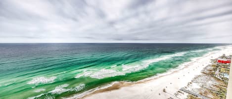 A beach with clear turquoise waters, a sandy shore, and a pier extending into the sea.
