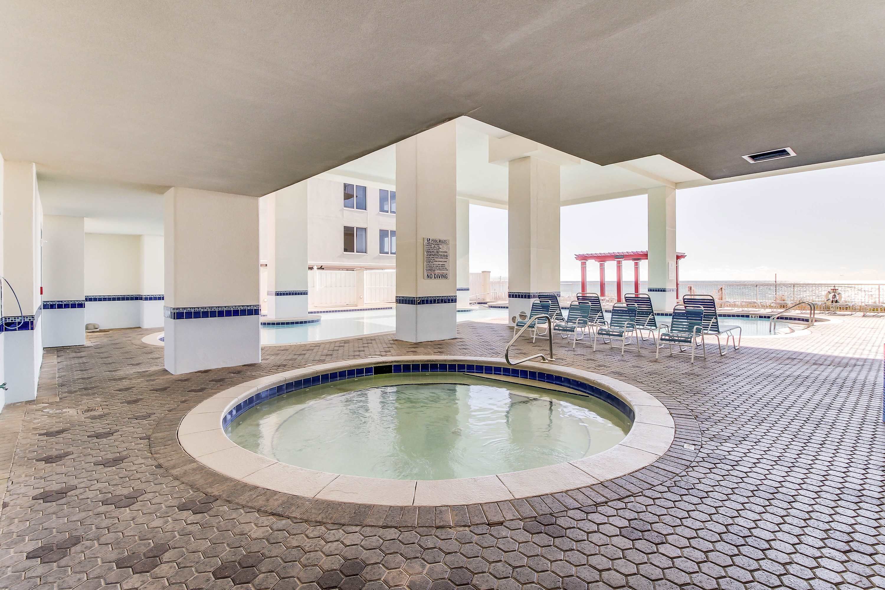 A pool area with a hot tub, lounge chairs, and a view of the sea.