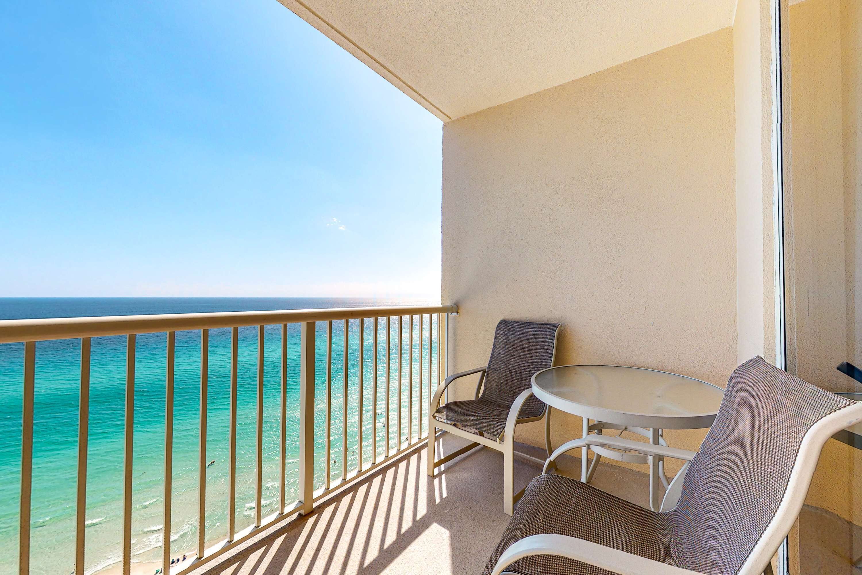 A balcony with a view of the ocean, a table, and two chairs.