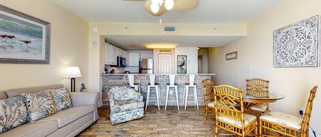 A living room with a sofa, a patterned armchair, a dining table with chairs, and a ceiling fan.