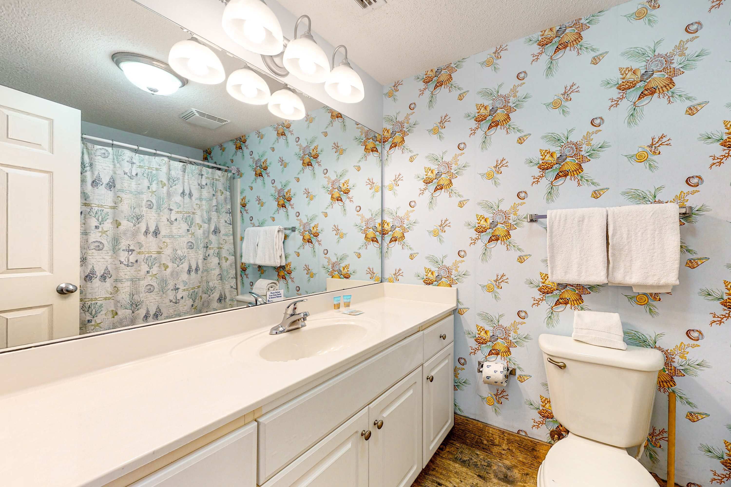 Een badkamer met een wastafel, spiegel en toilet. De muren zijn behangen met een bloemenpatroon.