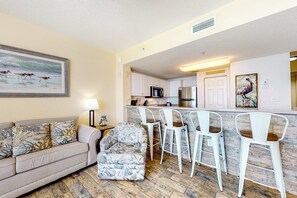 Ein Wohnzimmer mit einer Couch, einem gemusterten Sessel und einer Bar mit weißen Barhocker.