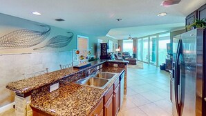 A spacious kitchen with granite countertops, stainless steel sinks, and a large refrigerator. - Stunning corner-condo with panoramic views, wraparound deck & beach access (Panama City Beach)