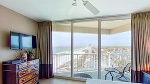 A hotel room with a large balcony, a TV, a dresser, and a bed. - Stunning corner-condo with panoramic views, wraparound deck & beach access (Panama City Beach)