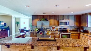 A kitchen with granite countertops, wooden cabinets, a stainless steel refrigerator, and a microwave. - Stunning corner-condo with panoramic views, wraparound deck & beach access (Panama City Beach)