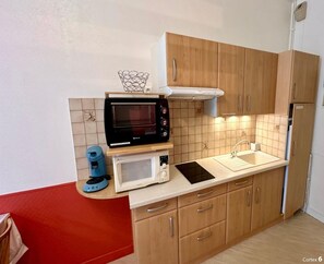 Ett kompakt kök med träskåp, en mikrovågsugn, en brödrost och ett handfat.