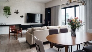 Ein modernes Wohnzimmer mit einer Couch, einem Esstisch, Stühlen, einem Flachbildfernseher und einer Zimmerpflanze.