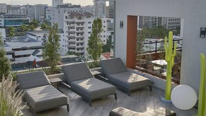 Eine Dachterrasse mit mehreren Sitzbereichen, darunter Sofas und Sessel, und Blick auf die Stadtlandschaft.