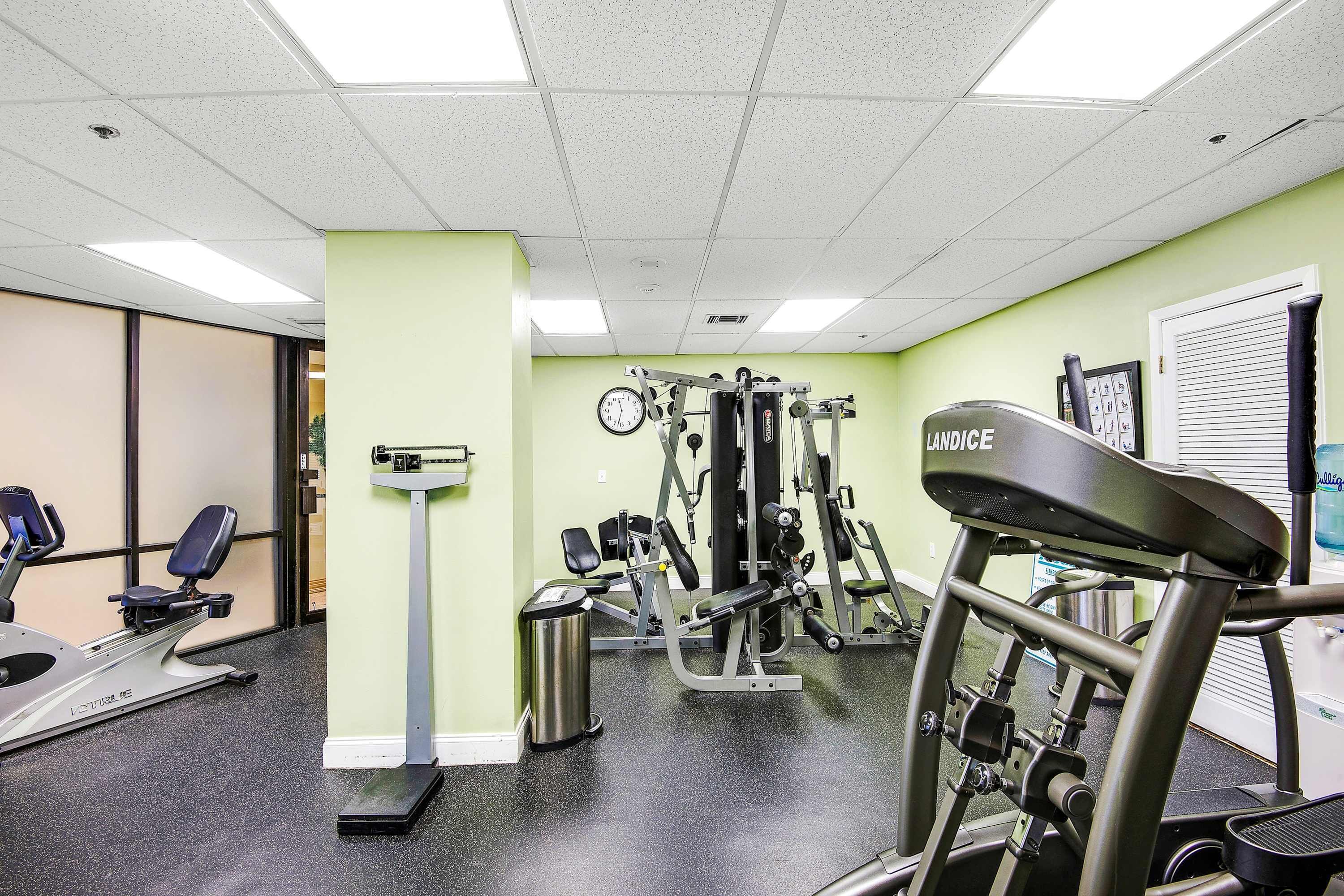 A gym with exercise equipment, a clock on the wall, and a trash can.