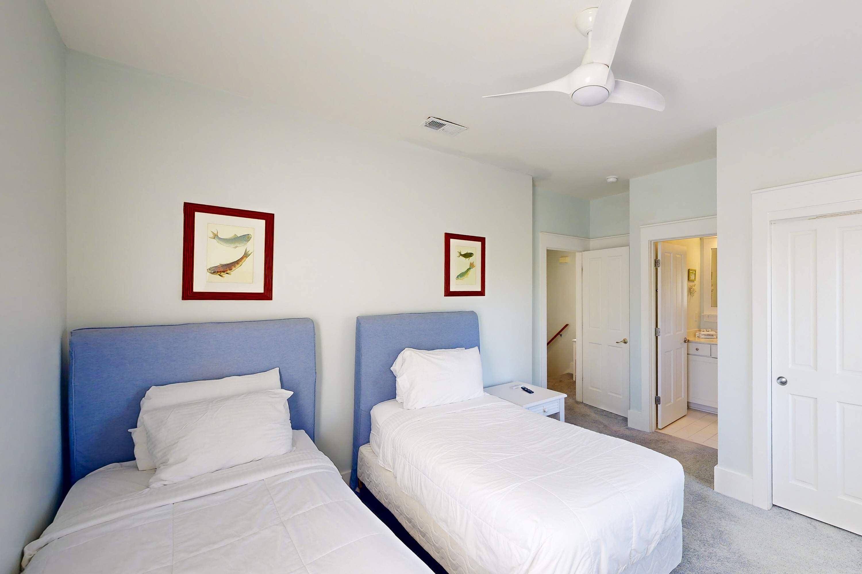 Ein Hotelzimmer mit zwei Betten, einem Deckenventilator und gerahmten Bildern an den Wänden.
