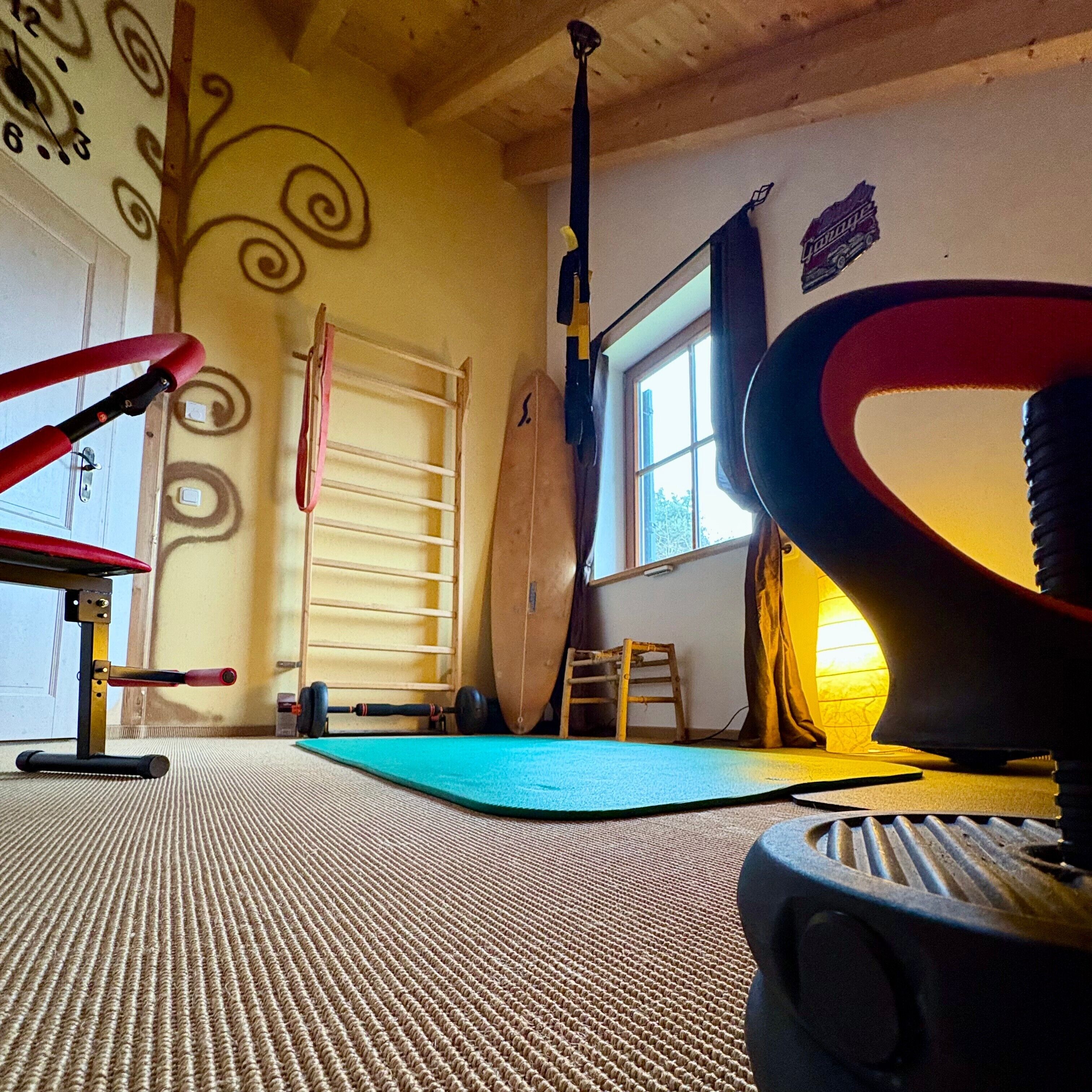 Een fitnessruimte met trainingsapparatuur, een pull-up stang, een yogamat en een raam met gordijnen.