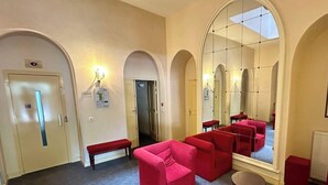 En hotelllobby med röda soffor, en bänk, en stor spegel och en dörr med en skylt.
