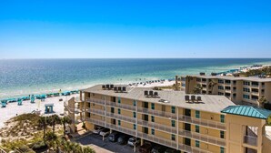 Ein Hotel direkt am Strand mit mehreren Etagen, einem Parkplatz und einem Strand mit Sonnenschirmen.