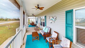A covered porch with wooden furniture, a teal-colored floor, and a view of a grassy area.