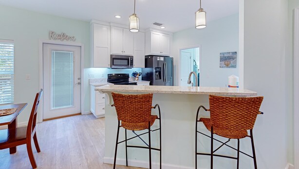 A modern kitchen with white cabinets, a central island with bar stools, a microwave, and a refrigerator.