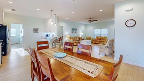 A spacious living area with a dining table, chairs, a ceiling fan, and a clock on the wall.