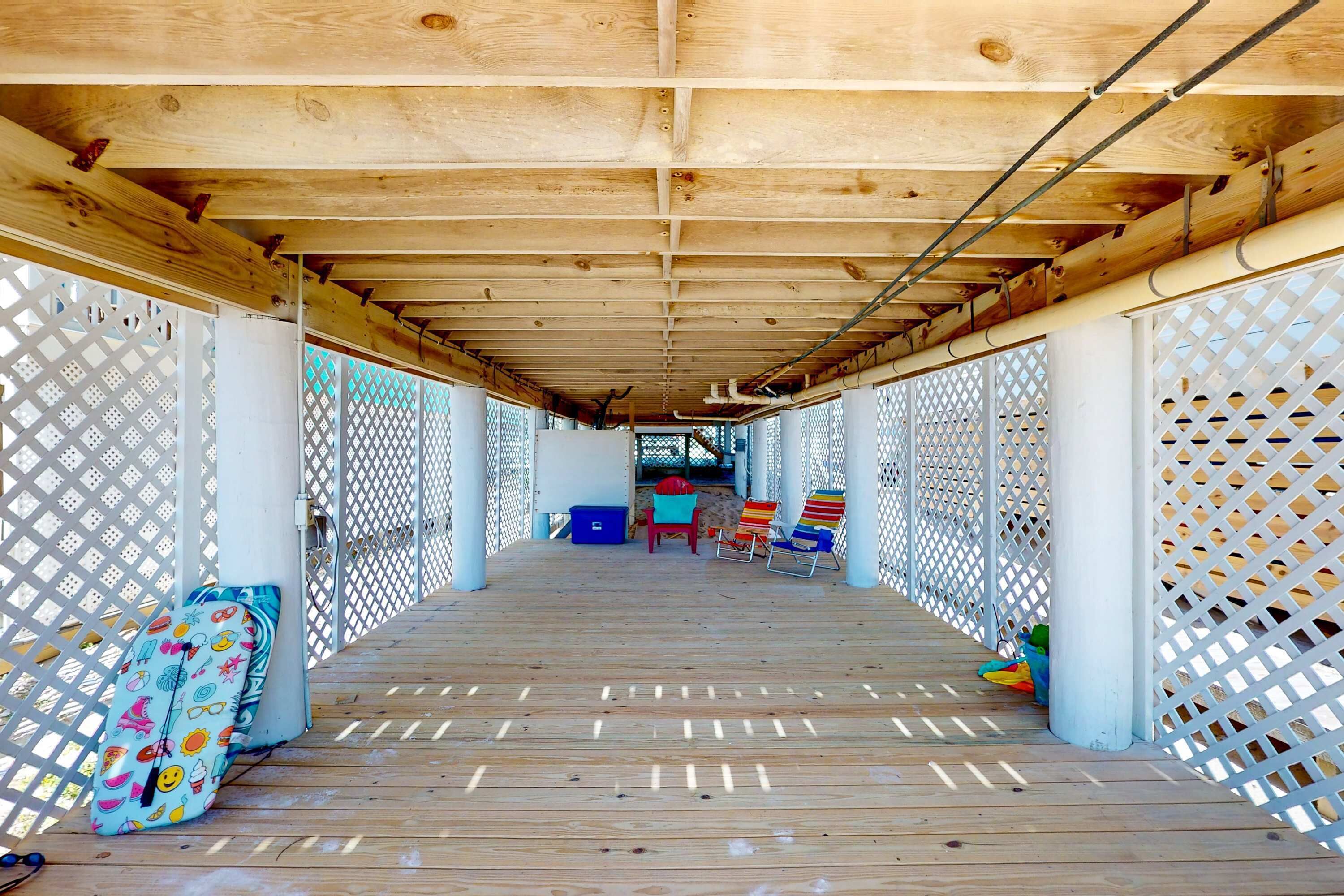 A covered wooden deck with a lattice fence, a blue storage box, and colorful chairs.