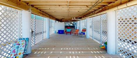 A covered wooden deck with a lattice fence, a blue storage box, and colorful chairs.