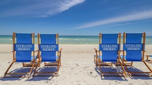 Vier blauwe strandstoelen met borden met de tekst 'Sterling Shores' op een zandstrand.