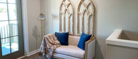 Een kamer met een lichtkleurige bank, twee blauwe kussens en een decoratief houten object aan de muur.