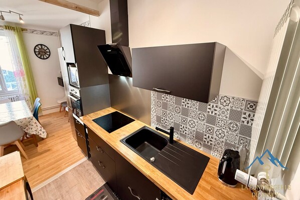 A modern kitchen with a black countertop, two sinks, a built-in oven, and a patterned backsplash. - Alpine sanctuary by the market lane (Mont-Dore)