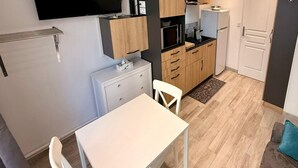 A compact kitchen with a flat-screen TV, wooden cabinets, a microwave, and a refrigerator. - Alpine sanctuary by the market lane (Mont-Dore)